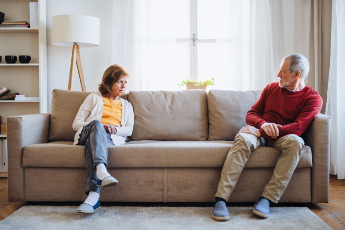 a-senior-couple-sitting-on-a-sofa-at-home-having-a-94WHQUJ